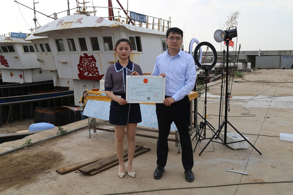 海鮮電商張夢琴與幫辦員手持食品經(jīng)營許可證合影。贛榆區(qū)委宣傳部供圖