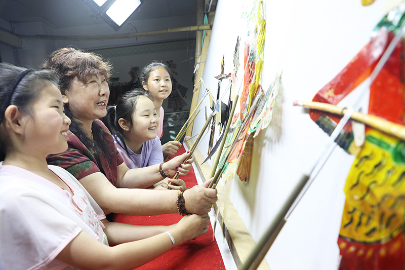 皮影藝人指導(dǎo)小朋友表演皮影戲。