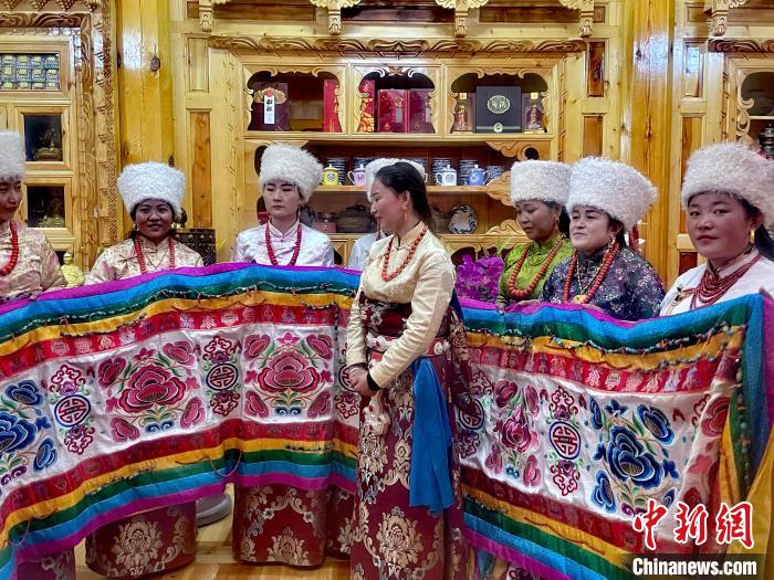 圖為女性展示村民自發(fā)繡制的“百米五彩哈達(dá)”?！±钣穹?攝